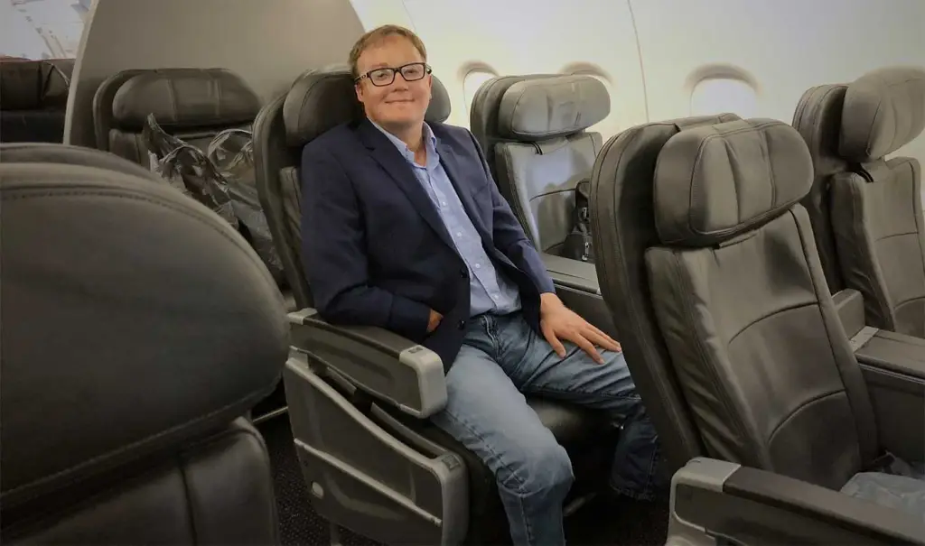 photo of John Morris a triple amputee sitting in an airline seat wearing a blue blazer an open collared blue shirt