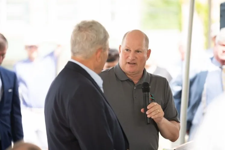 photo of Charles Hammerman at the opening of the Schoolhouse Hotel. He is wearing a brown grey polo shirt and holding a microphone