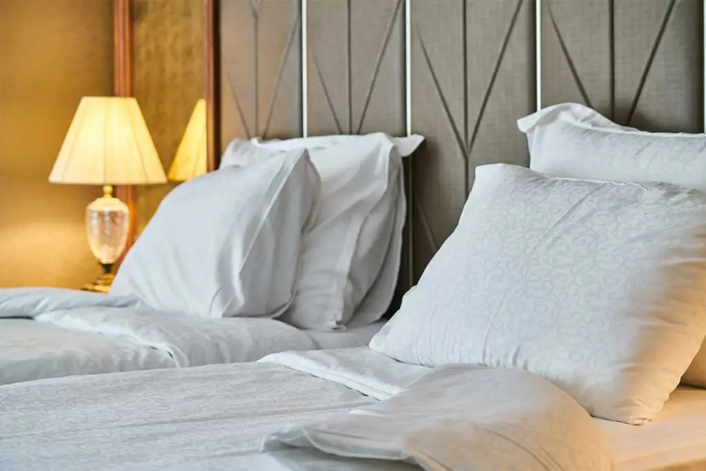 photo of a hotel bed with large white pillows propped against an upholstered headboard